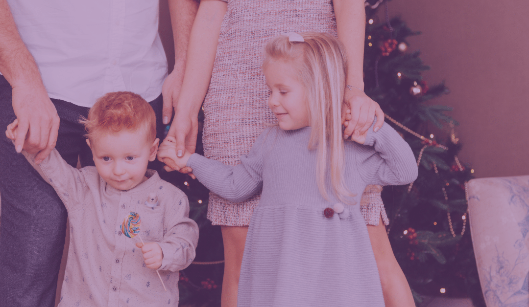 Two young children standing in front of and holding hands with their parents.