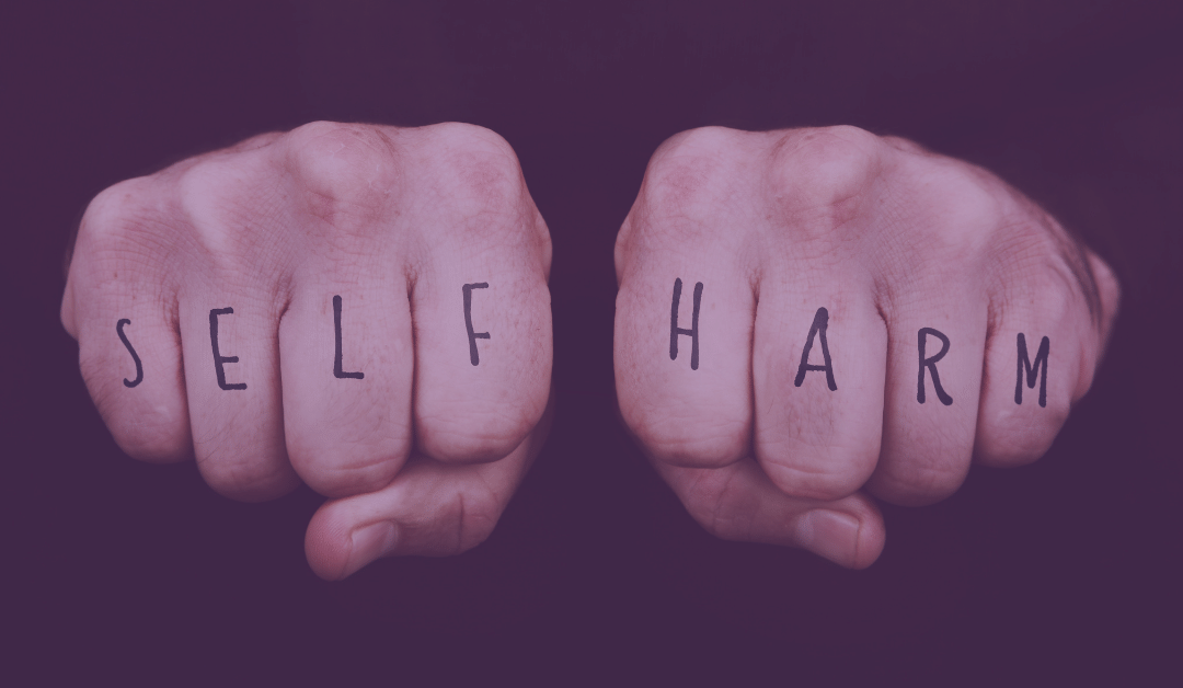 Two hands in fists with the words 'self harm' written on the fingers