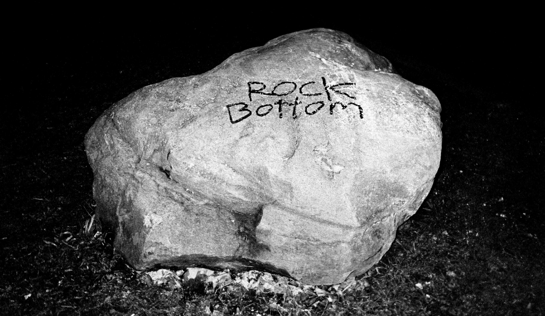 Black and white picture of a large rock with the words 'Rock Bottom' spray painted on the rock.