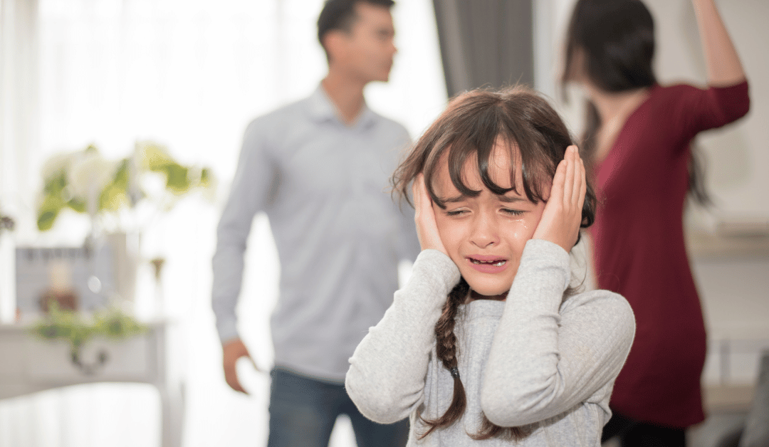 Child covering her ears and crying while her parents argue in the background.